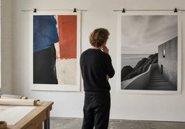 An artist comparing a textured abstract fine art print with a black-and-white architectural photo print in a bright studio.