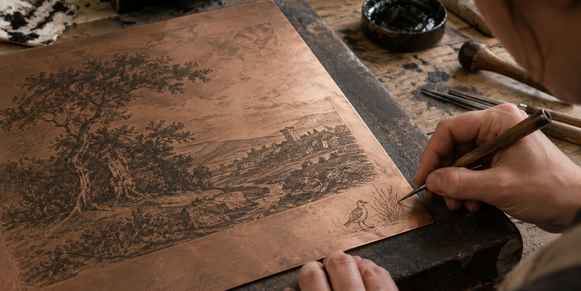 A printmaker incises a small bird-and-plant sketch in the margin of a copper plate beside a larger landscape.