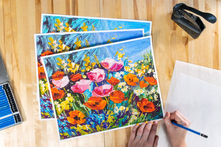 Prints being signed on a wooden background with pencils and embosser next to the prints.