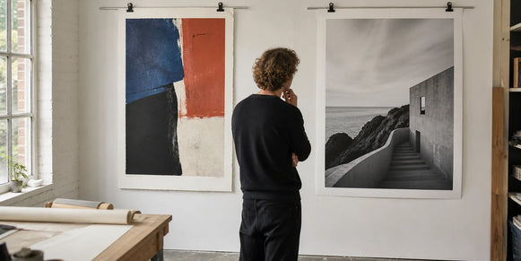 An artist comparing a textured abstract fine art print with a black-and-white architectural photo print in a bright studio.