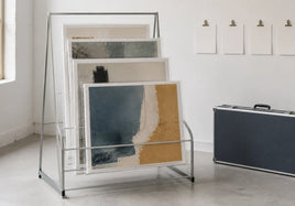 Four protected abstract art prints in a studio rack beside blank planning cards and a travel case.