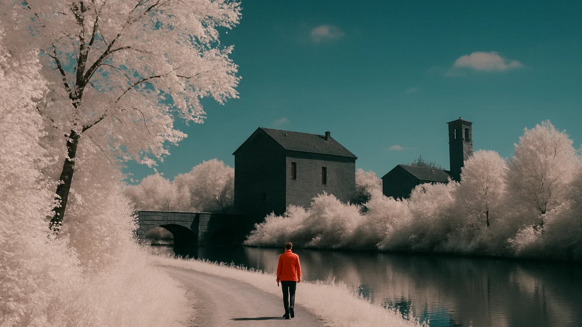 False-color infrared landscape with pale foliage, a teal sky, dark buildings, and a figure in a warm red jacket.