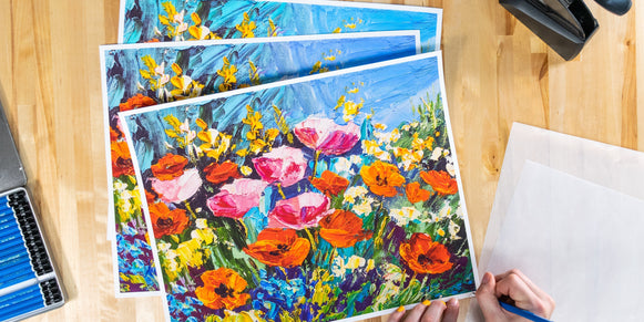 Prints being signed on a wooden background with pencils and embosser next to the prints.