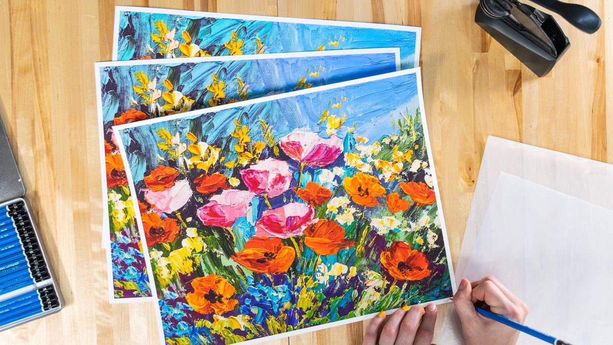 Prints being signed on a wooden background with pencils and embosser next to the prints.