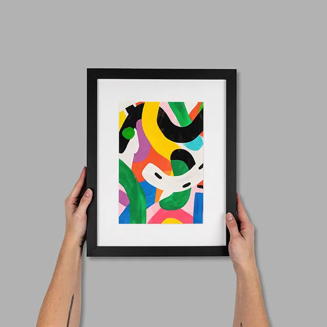 Hands holding a black framed print with colorful abstract artwork and a white mat